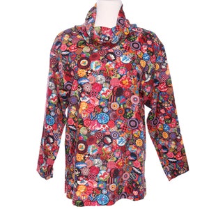 Op de afbeelding: Een tuniek met lange mouwen en een col, met een levendig, veelkleurig patroon van cirkelvormige ontwerpen. De dominante kleuren zijn rood, roze, blauw en geel, waardoor een patchwork-effect ontstaat. De tuniek wordt gepresenteerd op een witte mannequin.