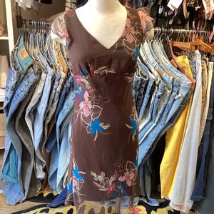 Puede incluir: Un vestido marrón de estampado floral con una superposición transparente. El vestido tiene un escote en V y mangas cortas. El vestido está en un maniquí en una tienda de ropa.