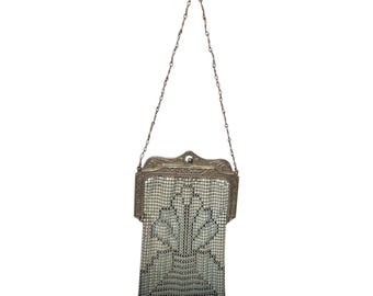 May include: A vintage silver-toned metal mesh purse with a chain handle. The purse features an ornate frame and a delicate, patterned mesh body. The design includes a stylized floral motif, and the purse is suspended from a delicate chain.