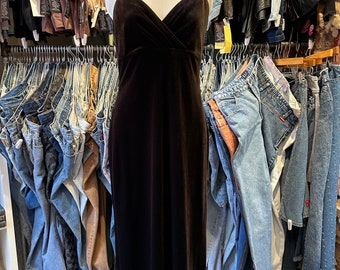 Può includere: Un abito maxi in velluto nero con sottili spalline a spaghetti. L'abito ha una scollatura a V e una silhouette aderente.