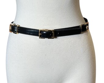 May include: Black belt with gold-colored rectangular buckle and accents. The belt is made of a shiny, patent leather-like material. The belt is displayed on a white mannequin.