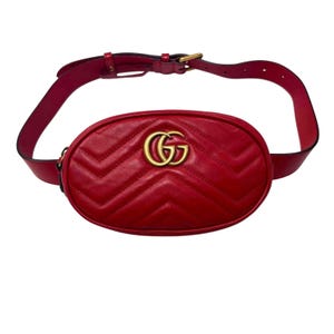 May include: A red leather belt bag with a quilted design. The bag features a gold-colored double G logo and a matching red belt. The bag is designed to be worn around the waist.