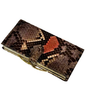 May include: A rectangular wallet featuring a textured snakeskin pattern in shades of brown, black, and cream with a prominent orange patch. The wallet includes a gold-toned metal frame closure and a matching snakeskin-covered tab snap fastener.