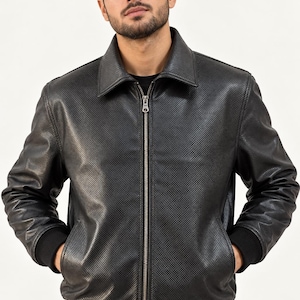 Peut inclure: Une veste noire avec un motif texturé en forme de grille sur toute la surface. La veste présente un col classique, une fermeture éclair métallique argentée sur toute la longueur, des manches longues avec des poignets côtelés noirs.
