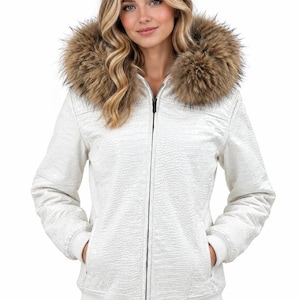 May include: A white zip-up jacket featuring a textured crocodile-embossed pattern, a full-length front zip, ribbed cuffs and hem, and a large hood trimmed with thick, fluffy brown faux fur. The jacket has two side pockets and a fitted silhouette.