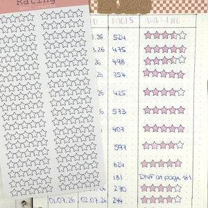 May include: A rectangular sticker sheet with a pink header labeled Rating and Anni creates, featuring two vertical columns of small black outlined star icons. The sheet is placed over a bullet journal page with a table tracking book ratings.