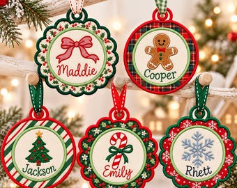 Op de afbeelding: Vijf ronde geborduurde kerstornamenten met feestelijke ontwerpen en namen. De ornamenten tonen een rode strik voor Maddie, een peperkoekmannetje voor Cooper, een kerstboom voor Jackson, een zuurstok voor Emily en een sneeuwvlok voor Rhett.