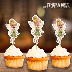 May include: Three cupcakes topped with Tinker Bell cupcake toppers. Each topper features a cartoon fairy with blonde hair in a bun, wearing a green dress and translucent wings. The text TINKER BELL CUPCAKE TOPPERS is printed in white at the top right.