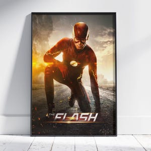 May include: A framed poster featuring The Flash in a red suit with a yellow lightning bolt emblem, kneeling on a dark road. The background shows a dramatic, cloudy sky with golden light. The text THE FLASH is printed in white at the bottom.