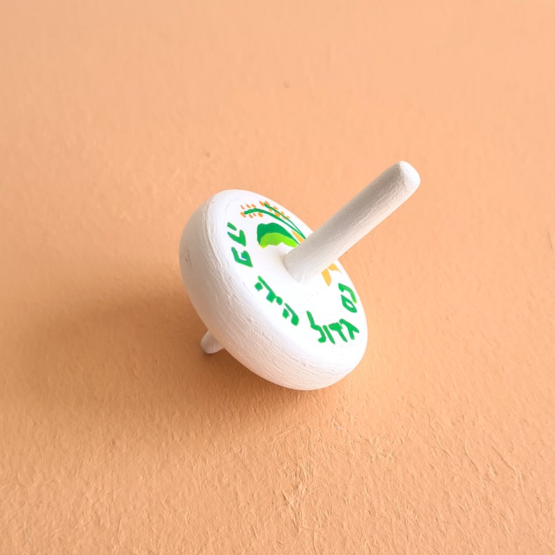 white wooden dreidel with orange flower green leaves and Nes Gadol Haya Po writing in green