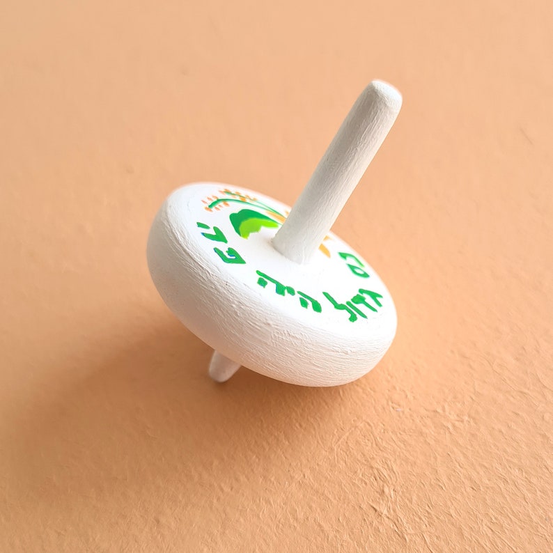 white wooden dreidel with orange flower green leaves and Nes Gadol Haya Po writing in green