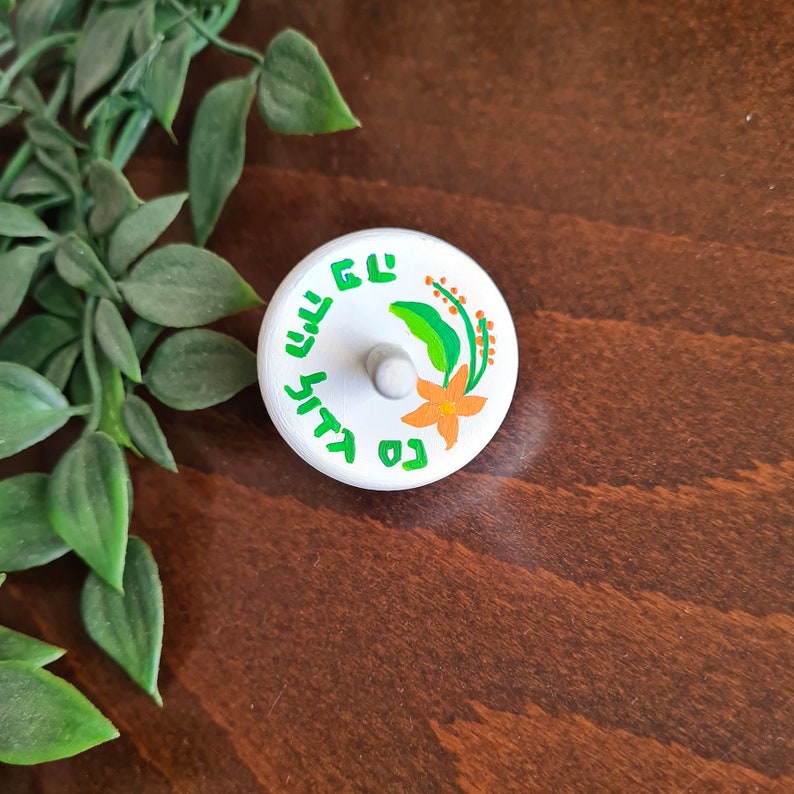 white wooden dreidel with orange flower green leaves and Nes Gadol Haya Po writing in green