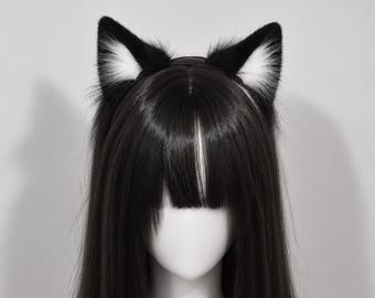 May include: A pair of black and white faux fur cat ears attached to a headband, worn on a mannequin head with long, straight black hair featuring blunt bangs. The ears are primarily black with white fur accents on the inner ear sections.