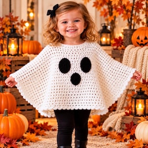 Può includere: Un poncho all'uncinetto bianco con un design a faccia di fantasma con due occhi ovali neri e una bocca ovale nera più piccola. Il capo presenta un bordo smerlato ed è indossato sopra leggings neri realizzati in filato testurizzato.