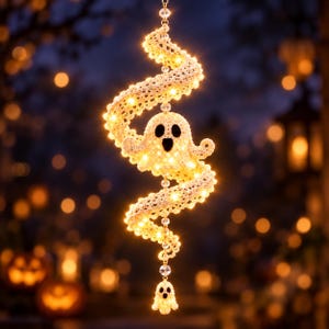 May include: A hanging crochet decoration featuring a cream-coloured ghost with black eyes and mouth, integrated into a spiralling, light-up ribbon structure adorned with small warm white LED lights and clear crystal beads, ending in a small ghost.