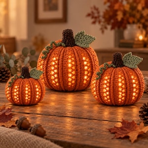 May include: Three crocheted orange pumpkins with dark brown stems and light green leaves. Each pumpkin features a textured ribbed pattern with star-shaped cutouts that emit a warm, glowing light from within, creating a festive seasonal display.