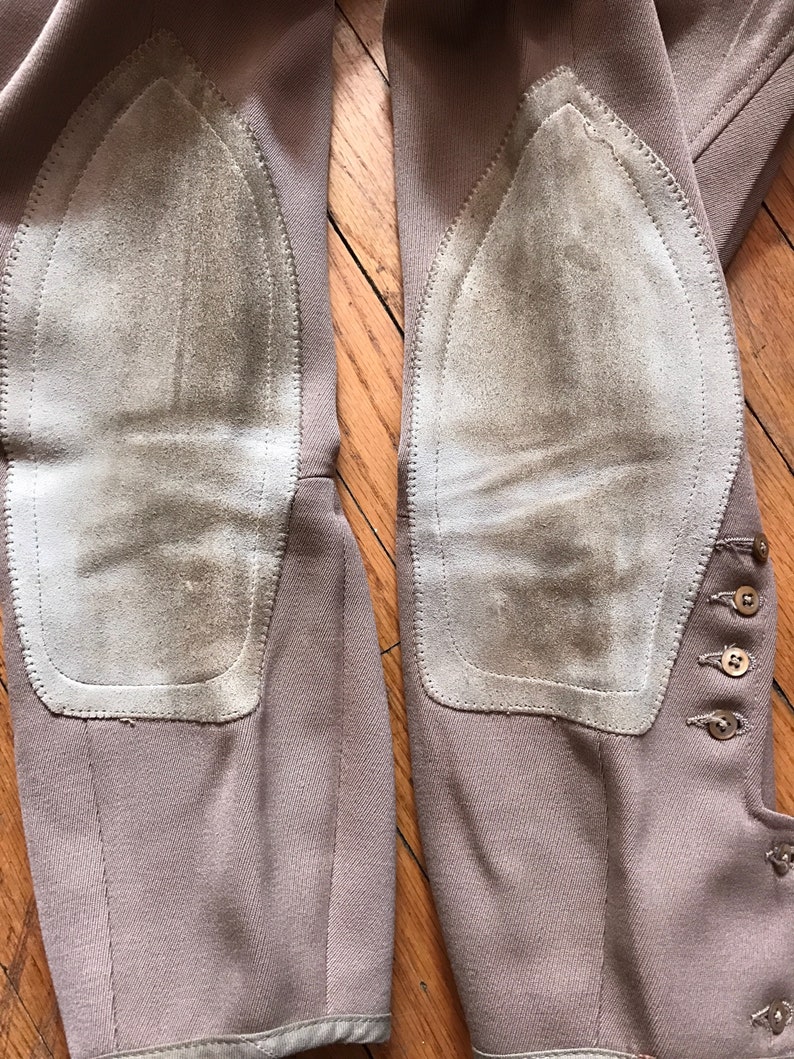 May include: A pair of brown riding breeches with suede knee patches. The breeches have a button closure on the side.