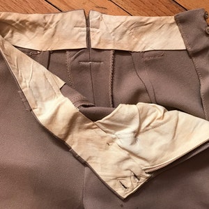 May include: A pair of brown pants with a zipper and button closure. The pants have a white lining and are turned inside out to show the lining.