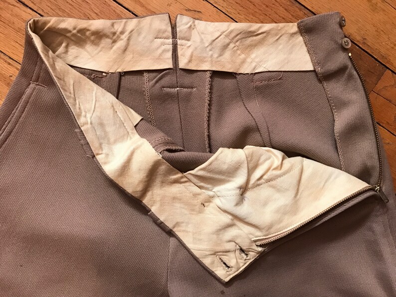 May include: A pair of brown pants with a zipper and button closure. The pants have a white lining and are turned inside out to show the lining.