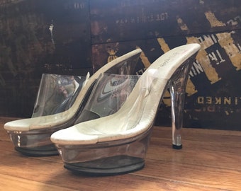 May include: A pair of clear plastic high-heeled shoes with a white platform and a thin strap. The shoes have a stiletto heel and are made of clear plastic.