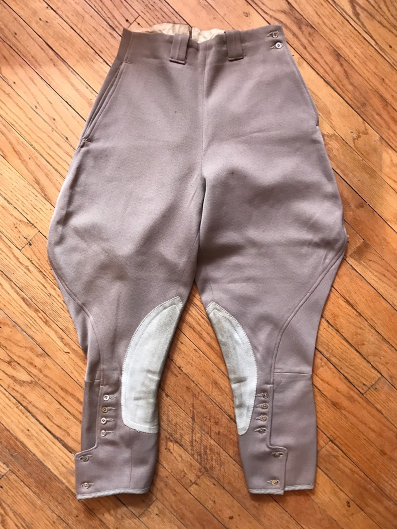 May include: A pair of beige riding breeches with white leather knee patches and button closures at the bottom of the legs.