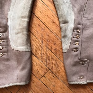 May include: A pair of brown riding breeches with suede knee patches and multiple button closures on the sides. The breeches have a white trim around the bottom.