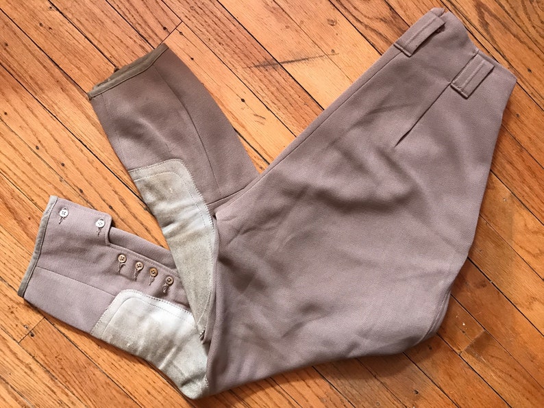 May include: A pair of brown riding breeches with knee patches and button detailing on the legs.