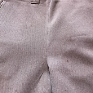 May include: A pair of light brown pants with a button fly and belt loops. The pants are made of a smooth, woven fabric.