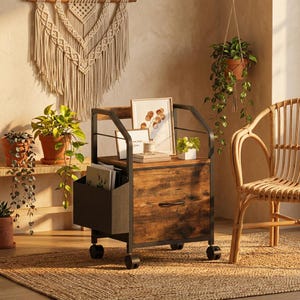 May include: A mobile filing cabinet with a rustic brown wood-grain finish and a black metal frame. It features a single drawer with a curved handle, a top surface for display, and a side storage pocket made of grey fabric, all set on four wheels.