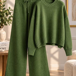 May include: A matching olive green two-piece set consisting of a long-sleeved sweater and wide-leg trousers. The sweater features a ribbed crew neckline and cuffs. The trousers have an elasticized waistband with a drawstring and side slits.