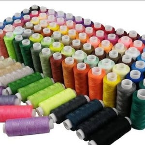 Puede incluir: Una gran colección de carretes de hilo de coser dispuestos en un patrón de cuadrícula. Los carretes presentan una amplia variedad de colores vibrantes, incluyendo tonos de rosa, morado, verde, naranja, amarillo, azul, negro, blanco y neutros.