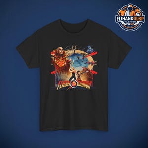 Puede incluir: Una camiseta negra de manga corta con un estampado gráfico colorido de la película Flash Gordon. El diseño muestra personajes, un castillo y el texto FLASH GORDON en letras amarillas negritas con un emblema circular rojo reemplazando la letra O.