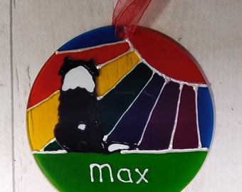 May include: Round glass ornament with a black and white dog silhouette against a rainbow background. The dog is facing away from the viewer and the ornament has the name "max" written in white on a green background.