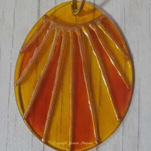 May include: A round, yellow and orange glass pendant with a gold sun design. The pendant is hanging from a gold chain.