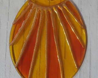 May include: A round, yellow and orange glass pendant with a gold sun design. The pendant is hanging from a gold chain.