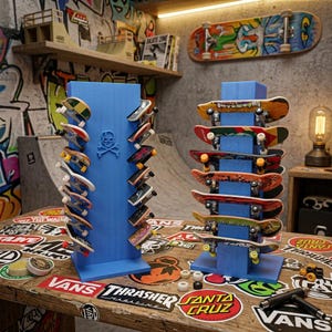 May include: Two blue vertical display stands holding multiple fingerboards. The left stand features a skull and crossbones emblem and holds fingerboards on both sides. The right stand holds fingerboards stacked horizontally on its front face.