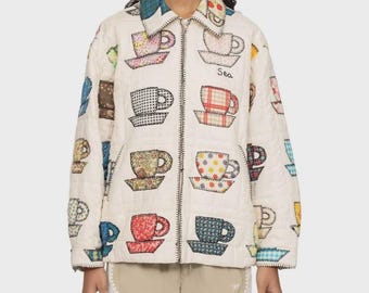 Peut inclure: Une veste zippée matelassée de couleur crème ornée d'un motif répétitif de tasses à thé aux couleurs et imprimés variés. Le mot Sea est brodé en fil noir sur la poitrine gauche. La veste possède un col et des manches longues.