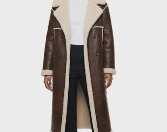 Peut inclure: Un long manteau marron foncé avec une doublure et des bordures en fausse peau lainée crème. Le manteau présente un large revers, une fermeture à double boutonnage et des manches longues avec des poignets en peau lainée.