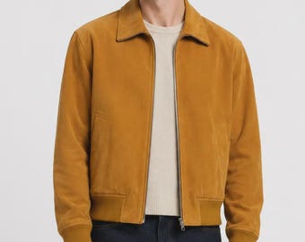 Peut inclure: Un blouson bomber en daim jaune moutarde avec un col classique, une fermeture éclair métallique argentée sur toute la longueur, ainsi que des poignets et un ourlet côtelés. Porté sur un pull en maille texturée crème et un jean bleu foncé.