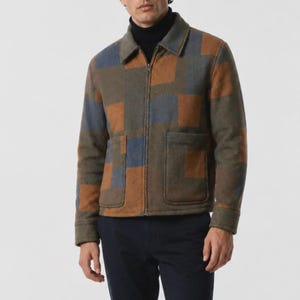 Peut inclure: Une veste zippée présentant un motif à grands carreaux dans des tons marron, vert olive et bleu ardoise. La veste possède un col classique, des manches longues avec poignets et deux grandes poches plaquées à l'avant, portée sur un col roulé noir.