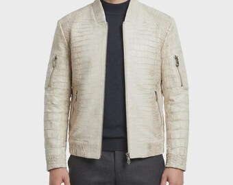 Peut inclure: Un blouson bomber couleur crème avec un motif texturé en peau de crocodile, une fermeture éclair intégrale sur le devant avec une tirette en forme de crâne et deux poches zippées sur la poitrine. Porté sur un pull à col montant bleu marine.