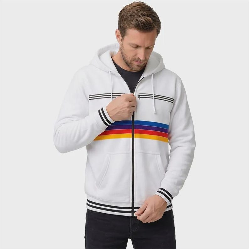 May include: A white zip-up hoodie featuring a horizontal rainbow stripe across the chest in blue, red, and yellow. The garment includes a drawstring hood, black zipper, and black and white striped ribbed cuffs and hem with matching chest accents.