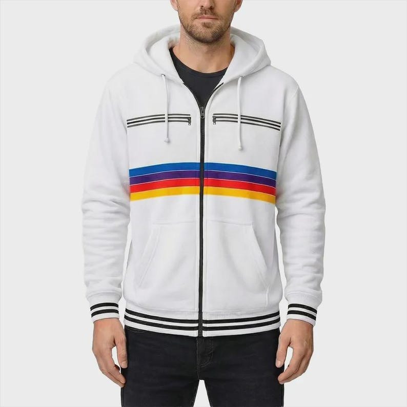 May include: A white zip-up hoodie featuring a horizontal stripe pattern in blue, purple, red, and yellow across the chest. The garment includes a black front zipper, two horizontal black zippered chest pockets, and black striped ribbed cuffs and hem.