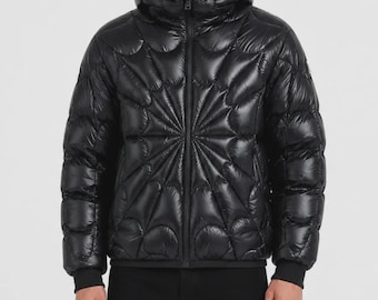 Peut inclure: Une doudoune noire à la finition brillante avec une capuche. La veste présente un motif matelassé distinct qui rayonne depuis le centre de la poitrine dans un design en toile. Elle possède une fermeture éclair frontale et des poignets côtelés.