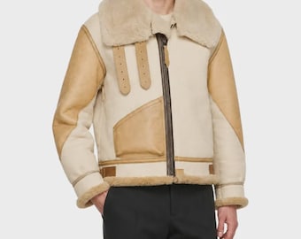 Peut inclure: Une veste en peau lainée crème et beige dotée d'un grand col en fourrure, d'une fermeture éclair marron foncé sur toute la longueur et de deux sangles à boucle verticales sur la poitrine. Elle présente des empiècements en cuir beige sur les manches.