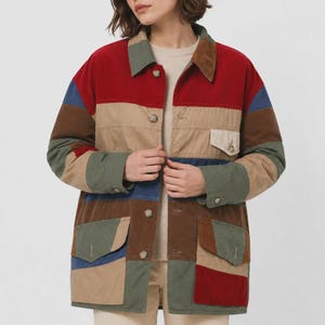 Può includere: Una giacca a maniche lunghe con bottoni caratterizzata da un design a blocchi di colore con pannelli orizzontali in rosso, beige, verde oliva, marrone e blu. La giacca include un colletto a punta, due ampie tasche applicate con patta e una tasca sul petto.