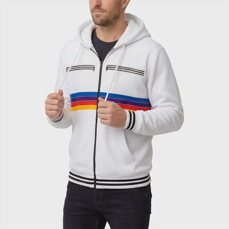 May include: A white zip-up hoodie featuring a horizontal multi-colored stripe pattern in blue, purple, red, and yellow across the chest. The garment includes two zippered chest pockets, a drawstring hood, and black and white striped ribbed cuffs.