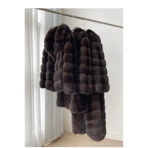 May include: Three dark brown, long-sleeved, textured coats with a thick, plush, layered appearance hanging on a metal rack. Each coat features a dense, soft-looking pile with horizontal segments, a high collar, and a full-length design.