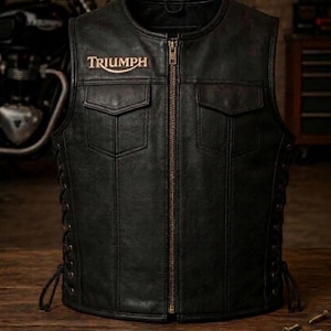 May include: A black leather vest featuring a central metal zipper, two chest pockets with flaps, and side lacing details. The word Triumph is embroidered in a light color on the upper right chest area of the garment, which has a round neckline.