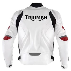 May include: A white motorcycle jacket featuring black side panels and red accents on the elbows. The back displays the black text TRIUMPH in a stylized font. The jacket includes a high collar, structured padding, and adjustable waist straps.